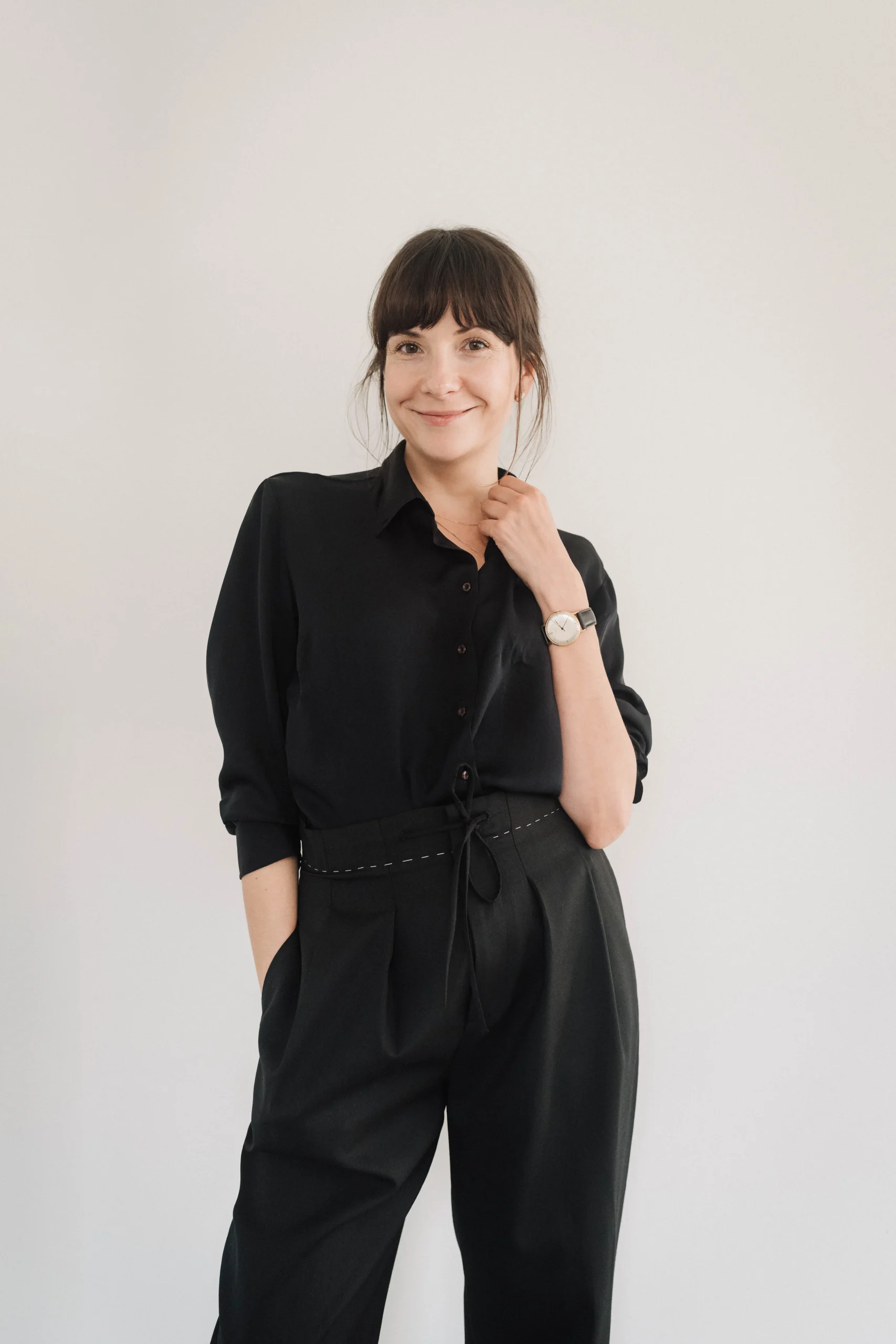 Julie Ermakow in schwarzer Bluse und schwarzer Hose vor einer hellen Wand.