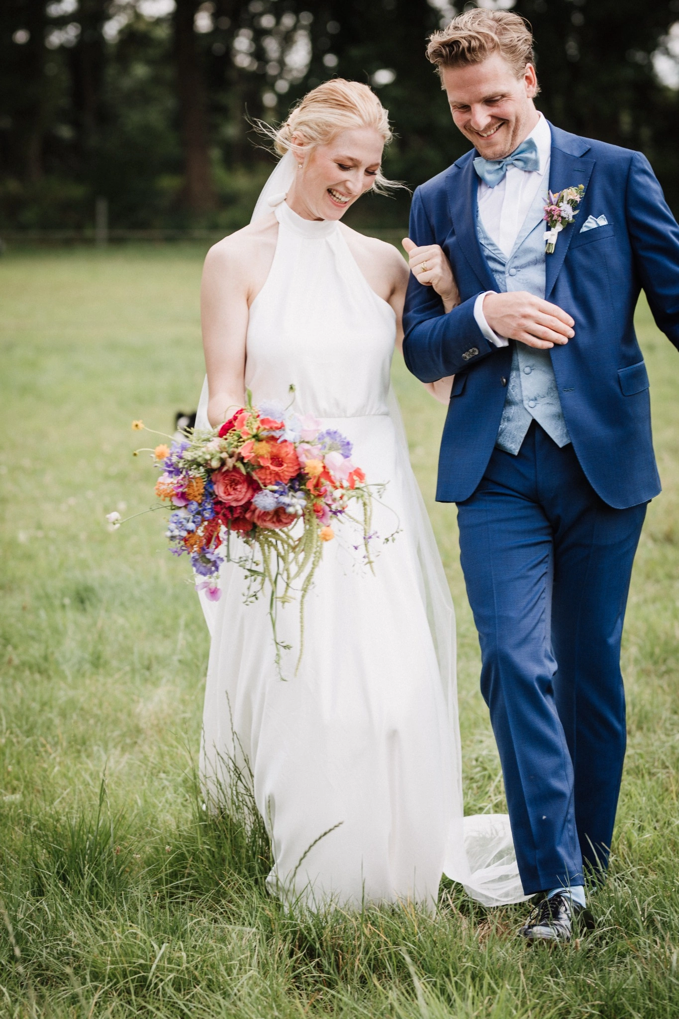 Lena und Lasse gehen gemeinsam über eine Wiese, mit einem bunten Brautstrauß.