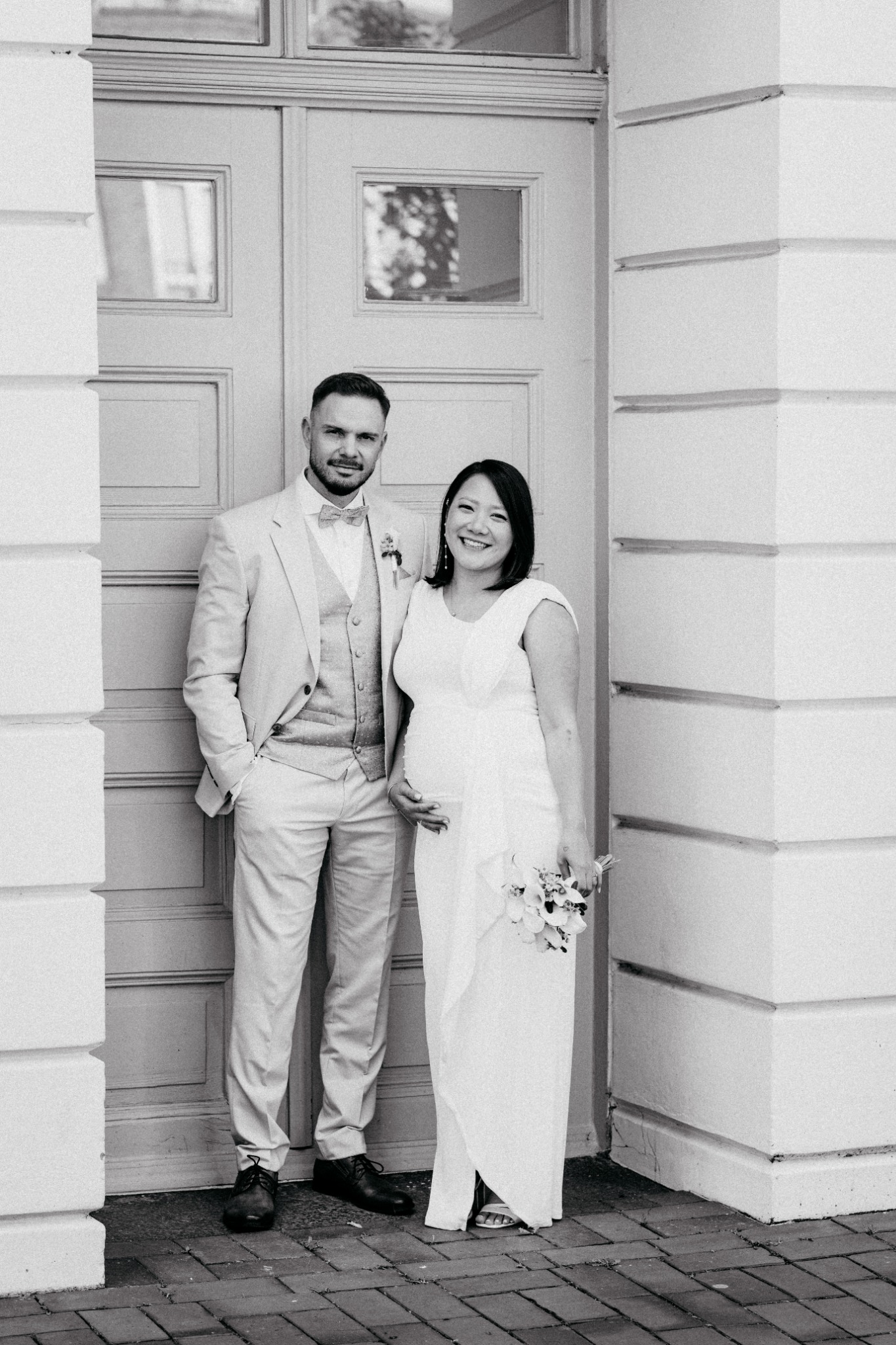 Hochzeitspaar vor einer hellen Tür, in Schwarz-Weiß.