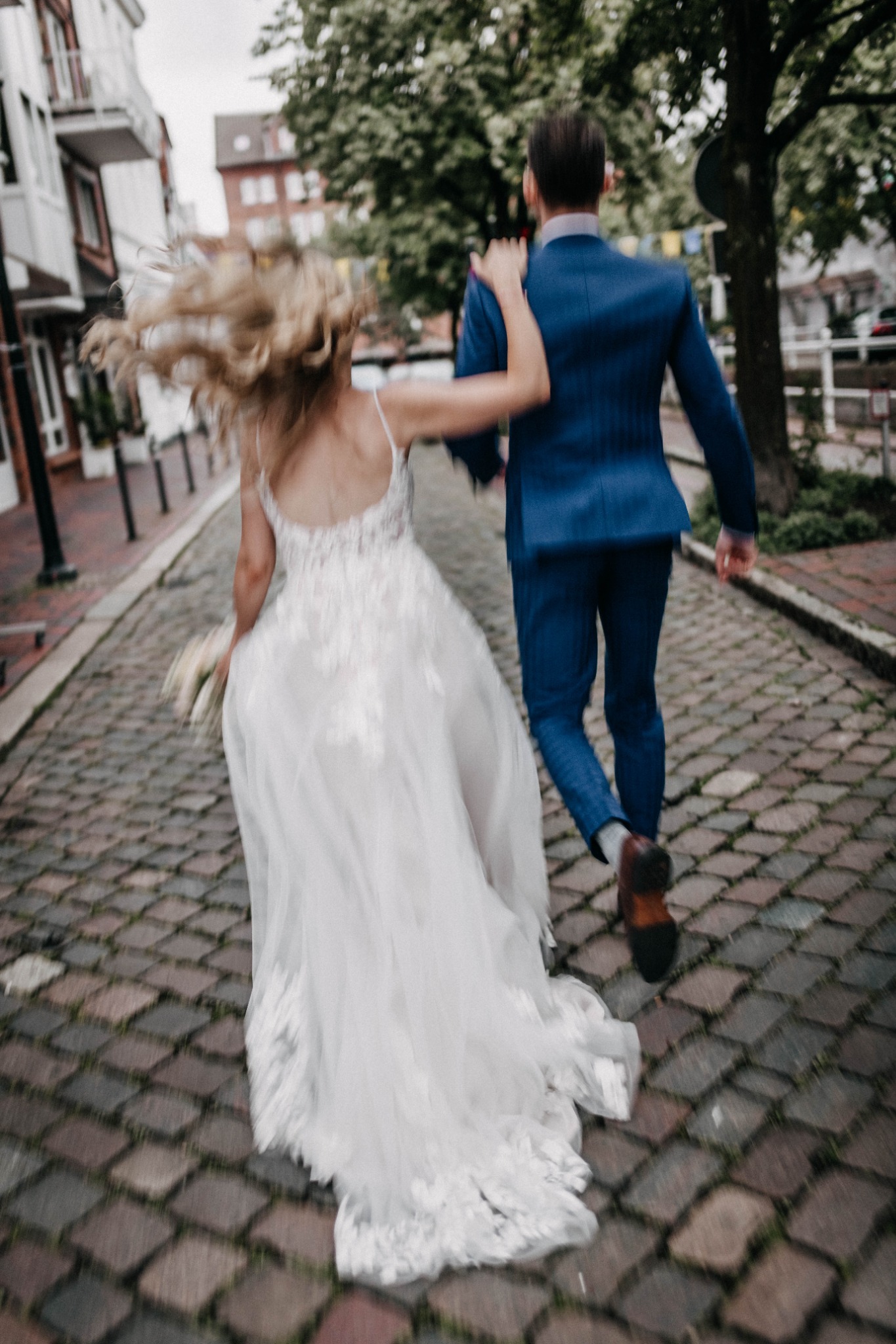 Ein Hochzeitspaar geht Hand in Hand durch eine Kopfsteinpflastergasse.
