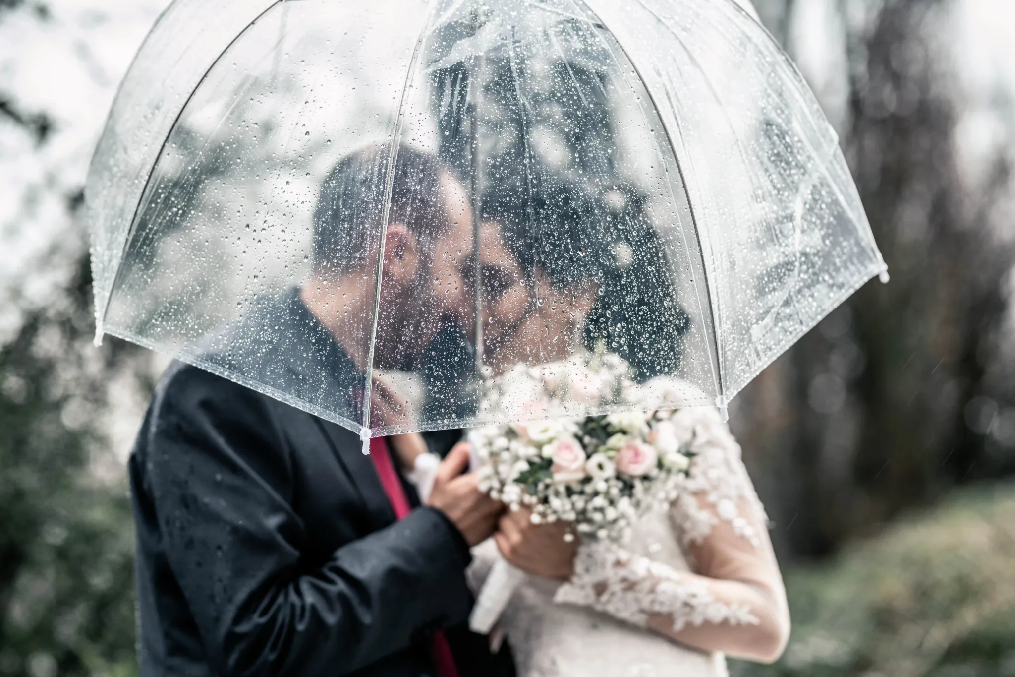 Ein Hochzeitspaar küsst sich unter einem transparenten Regenschirm.