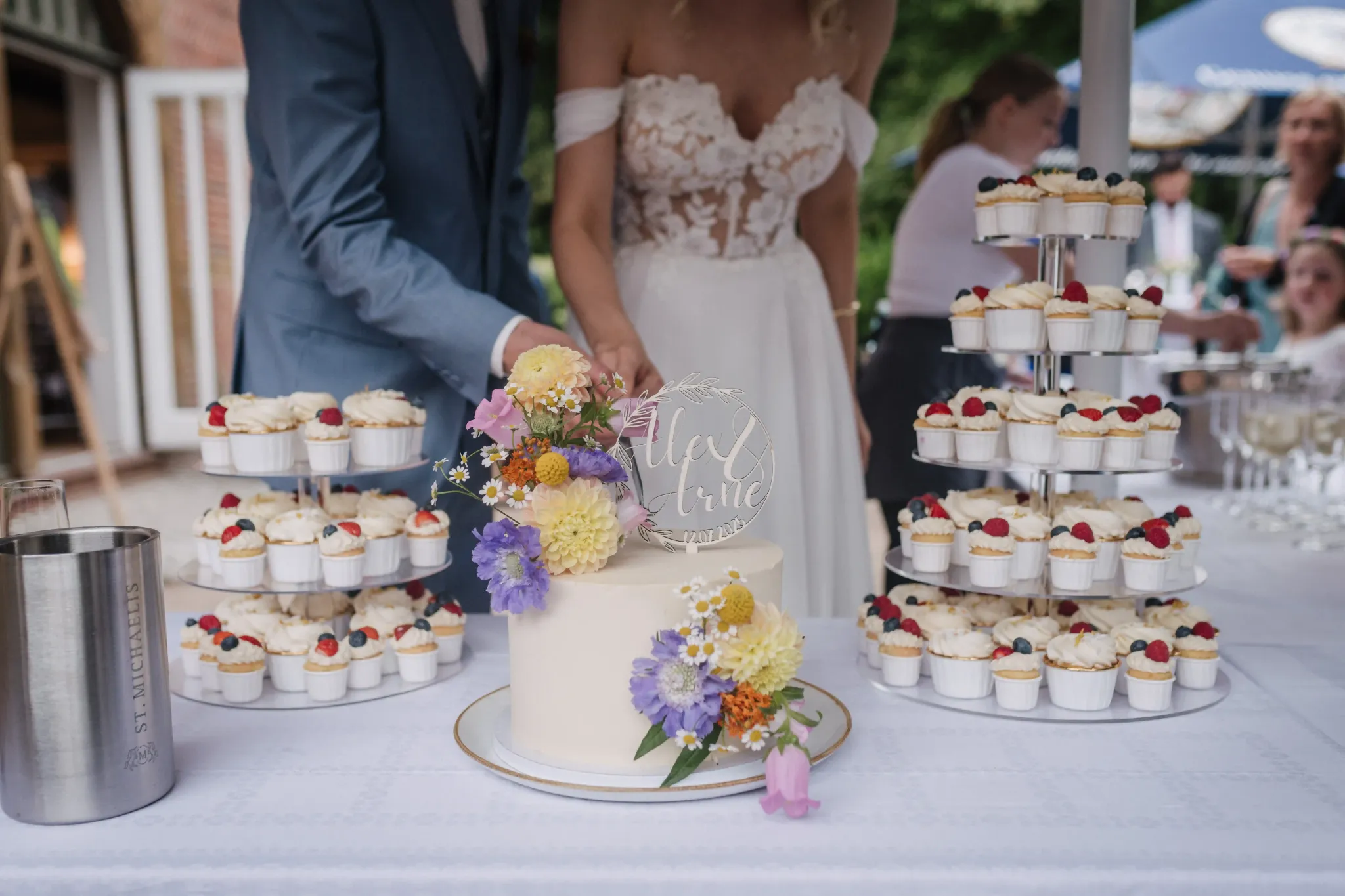 Hochzeitspaar an einem Tisch mit einer Etagere voller kleiner Törtchen.