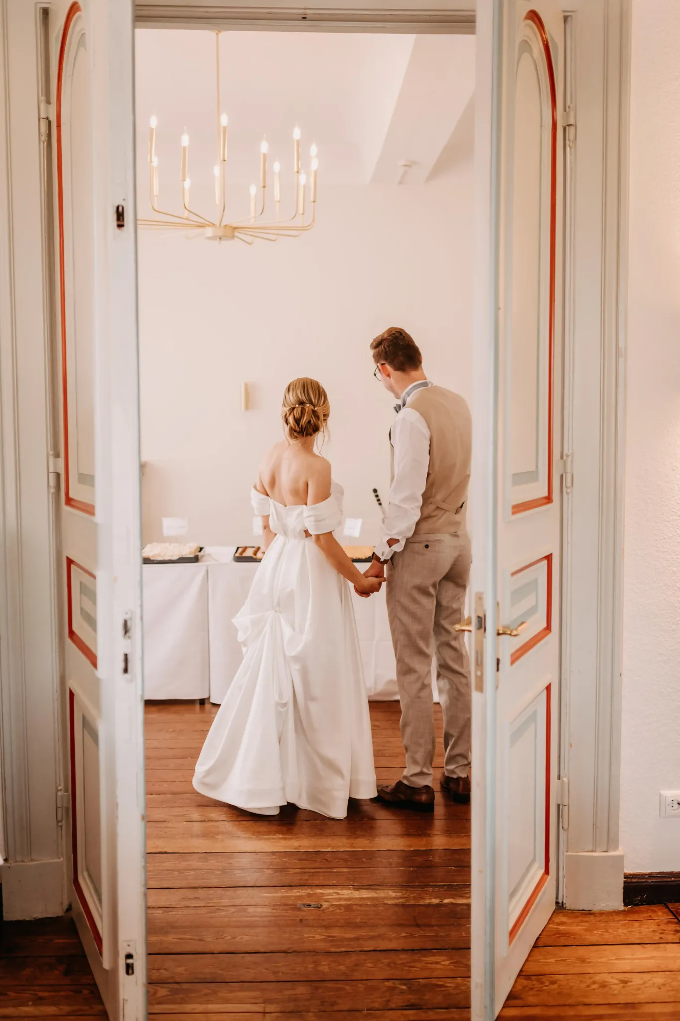 Hochzeitspaar im Türrahmen eines hellen historischen Zimmers.